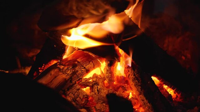 Slow motion of a burning fire in the night. Flames and wood. Red embers, smoke, ash and ash. A camping poster in the mountains. Close-up