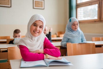 Group of happy Muslim school children sitting at the desk in the classroom. - obrazy, fototapety, plakaty