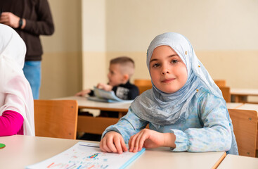 Group of happy Muslim school children sitting at the desk in the classroom.