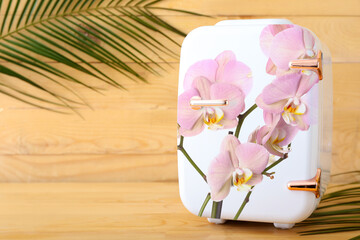 Stylish cosmetic refrigerator with floral print on wooden background