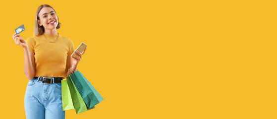 Pretty young woman with credit card, mobile phone and shopping bags on yellow background with space for text. Online shopping