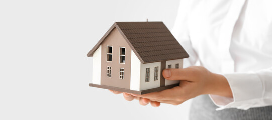 Real estate agent with house model on light background, closeup