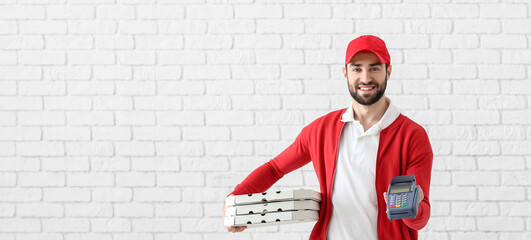 Delivery man holding cardboard pizza boxes and payment terminal on white brick background with space for text