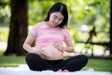 Asian happy pregnant woman in the garden and touching her belly. pregnancy, motherhood, people and expectation concept