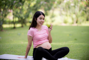 Happy pregnant Asian woman sitting on the lawn and touching her belly.Pregnancy, motherhood, people and expectations. X-ray sheet