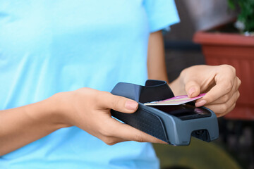 Woman paying with credit card via payment terminal in cafe, closeup