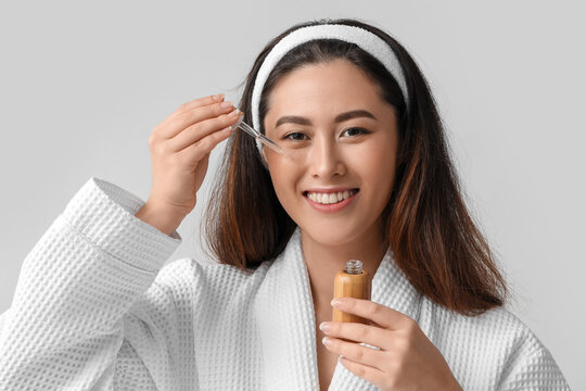 Young Asian woman with cosmetic serum on grey background