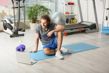 Sporty young man video chatting with coach in gym