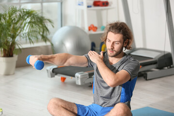 Sporty young man training with dumbbells  in gym