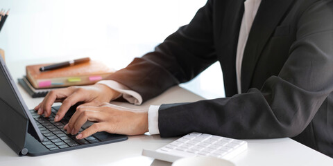 Close-up woman's hands work and typing on laptop computer with digital tablet on the desk at workplace.