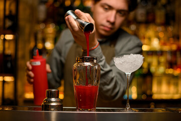 beautiful view of transparent glass shaker into which pours tomato juice from jigger and glass with...