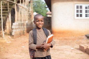 An African boy student wearing bag pack and holding book smiling and looking at camera