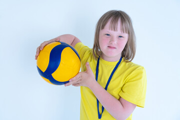 Portrait of a cute girl with blue eyes and blond hair with Down syndrome in a yellow T-shirt holds...
