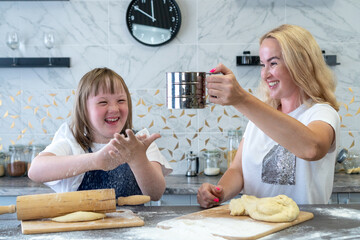 girl with down syndrome and her charming mother, bake dough pies in the kitchen 