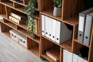 Wooden shelving unit with folders and houseplants near green wall