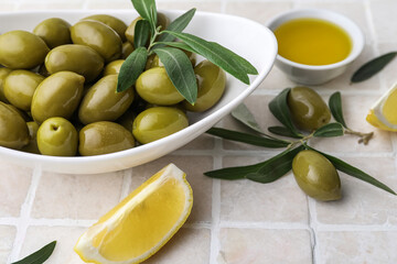 Bowl of green olives and lemon slice on color tile, closeup