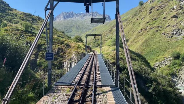 An old cog railroad runs over the mountains in Switzerland. The steam locomotive reminds of the old times. A bridge made of metal is crossed