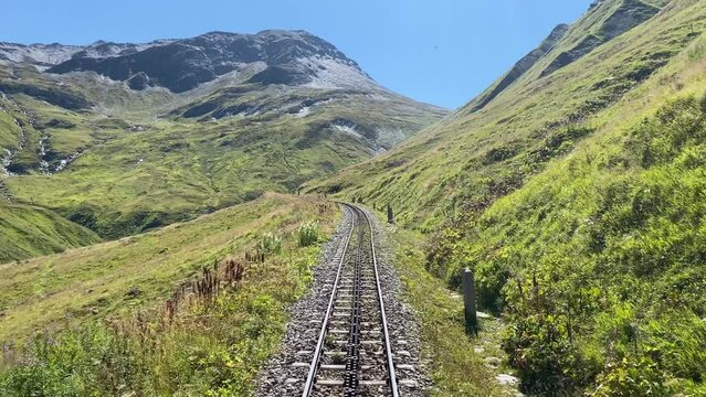 Steam railroad in the Swiss Alps goes over the Furka Pass with a rack railroad. The old railroad line runs high above the mountains