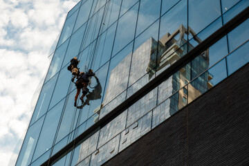 Workers cleaning office building windows. Industrial climbers wash the windows of a modern skyscraper. Men wash Windows on the evolution tower. Washers wash skyscraper windows sitting on hanging seats