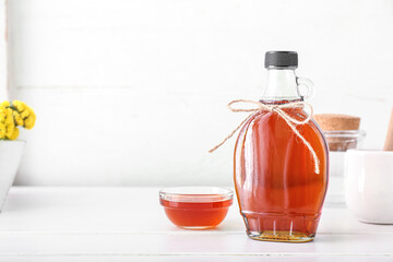 Glass bottle of maple syrup on light background