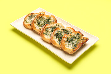 Plate with slices of toasted garlic bread on yellow background