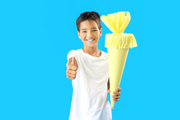 Little boy with yellow school cone showing thumb-up on blue background