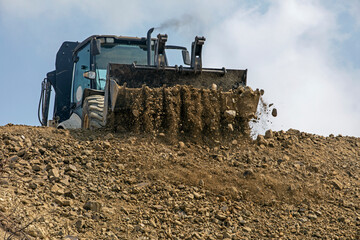 tractor with a big bucket aligns the road on a sunny hot day against the sky. Global construction. Mining, salt