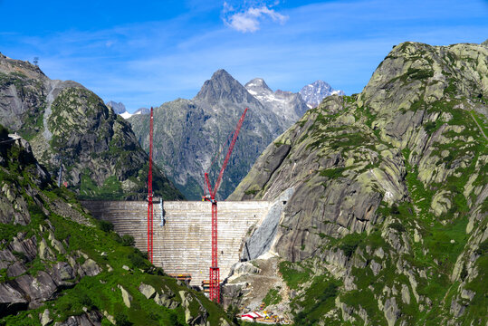 Scenic view of construction site with red cranes of new dam with lake at Swiss mountain pass Grimsel on a sunny summer day. Photo taken July 3rd, 2022, Grimsel Pass, Switzerland.