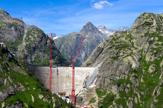 Scenic view of construction site with red cranes of new dam with lake at Swiss mountain pass Grimsel on a sunny summer day. Photo taken July 3rd, 2022, Grimsel Pass, Switzerland.