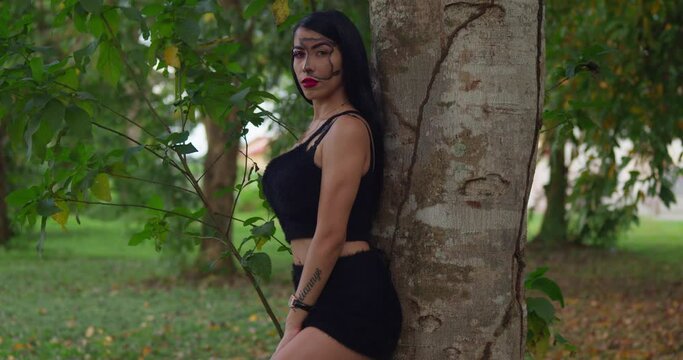A hispanic girl leans on a tree with a left pan camera movement while wearing face paint makeup