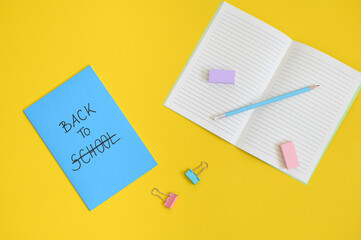 the text back to school written in the cover of a blue notepad, with the word school crossed out, on a bright yellow background