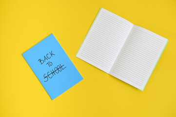 the text back to school written in the cover of a blue notepad, with the word school crossed out, on a bright yellow background