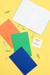 colorful back to school note with notebook and clip on yellow background