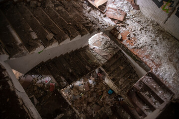 Circular staircase in Abandoned industrial building. Apocalyptic scene. Ruins of large factory covered with trash, junk, dirt and wooden furniture. Natural lighting.