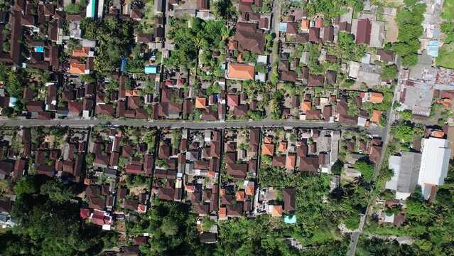 Balinese village aerial plan view, tiled roofs and typical house compounds, build along small straight road. Camera look straight down from height, flying along central street of MAS village