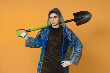 Young male gardener in a raincoat with a shovel on a colored background