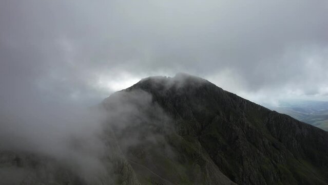 Big mountains in the clouds. Lake District by drone in 4K. Scafell Pike, highest mountain in England. Drone flying through clouds, dramatic reveal of climbers and hikers. Group of people on summit.
