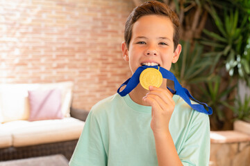 Cute child boy showing his gold medal standing on the terrace at home, outdoors.