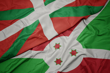 waving colorful flag of burundi and national flag of basque country.