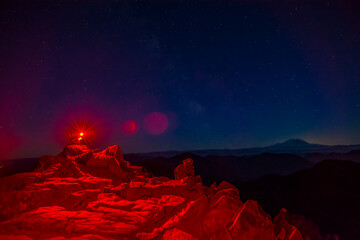 Athletic adventurous male hiker sitting on top of a mountain with a red headlamp shinning, looking...