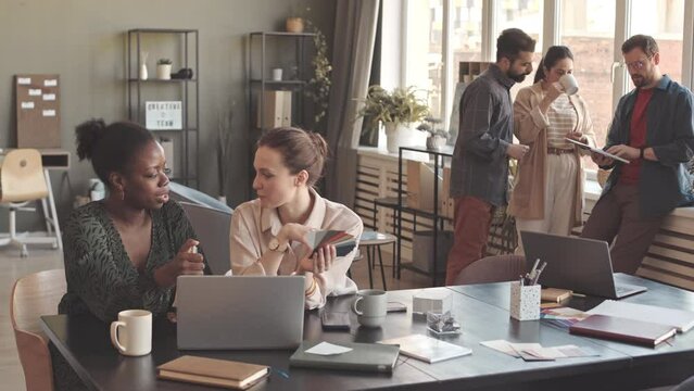 Medium slowmo of multiethnic team of colleagues discussing creative ideas for corporate project, working together in modern office
