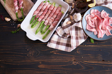 ceramic baking dish with aspargus covered with bacon on wooden kitchen table