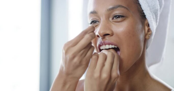 Happy, young and healthy female flossing teeth with dental floss in a bathroom looking in a mirror. Female taking care of her oral hygiene. Smiling lady doing her morning mouth routine.