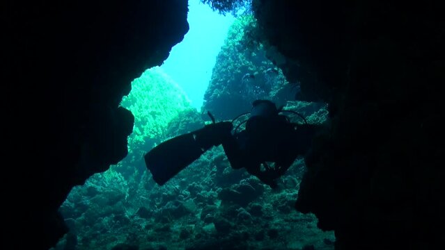 Scuba diver swimming through underwater cave with blue ocean in background