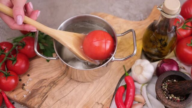 woman puts tomato to pot with hot boiling water for blanching