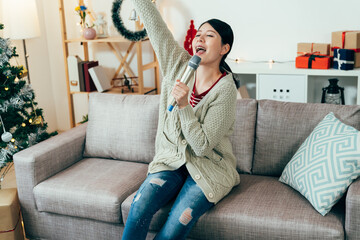 asian young lady holding microphone is singing an upbeat song alone at home. carefree winter...