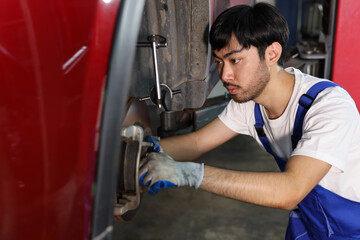 Fototapeta na wymiar Man technician car mechanic in uniform checking or maintenance a lifted car service at repair garage station. Worker holding wrench and fixing brake discs. Concept of car center repair service.