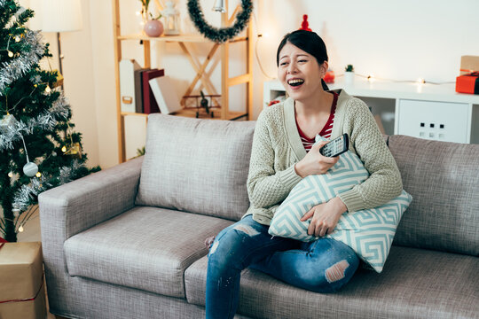 portrait chinese young lady holding pillow is bursting out laughing while she is streaming episodes on tv. Christmas, indoor recreation and lifestyle concept. genuine lifestyle