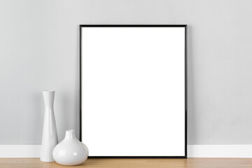 Elegant vertical black picture frame mockup, transparent template with white vases in front of light grey wall.