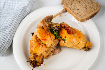 Baked rabbit thigh on plate, bread and towel on white plate.